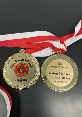 Médaille dorée à couronne de laurier montrant son avers illustré d’un écusson de service incendie et son revers gravé d’un remerciement pour quarante ans de service