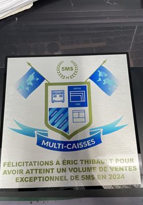 Plaque d’aluminium gravée d’un blason d’entreprise encadré de deux drapeaux, soulignant un volume de ventes
