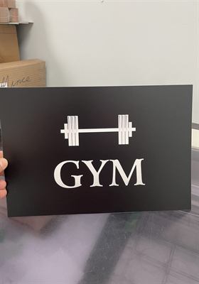 Panneau noir à lettrage et haltère découpés en blanc, indiquant un gymnase