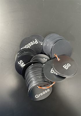 Lot de jetons ronds noirs gravés en blanc, identifiant différents fluides d’atelier, montés sur cordelettes