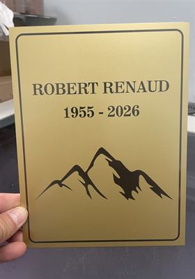 Plaque dorée gravée d’un nom, de dates et d’une silhouette de montagnes